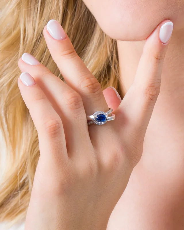 Bague à pierre bleue ovale entourée de petites pierres blanches, portée par une main posée sous le menton