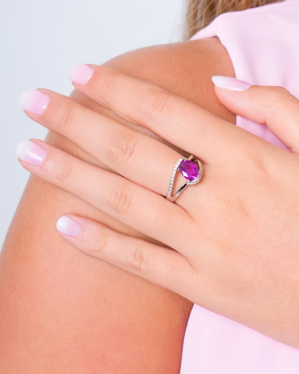 Bague à pierre ovale rose-violet sur un anneau croisé serti de petites pierres, main posée sur l'épaule