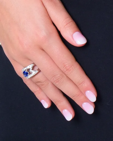 Bague en V pavée de petites pierres blanches avec une pierre bleue, sur une main posée sur une robe noire